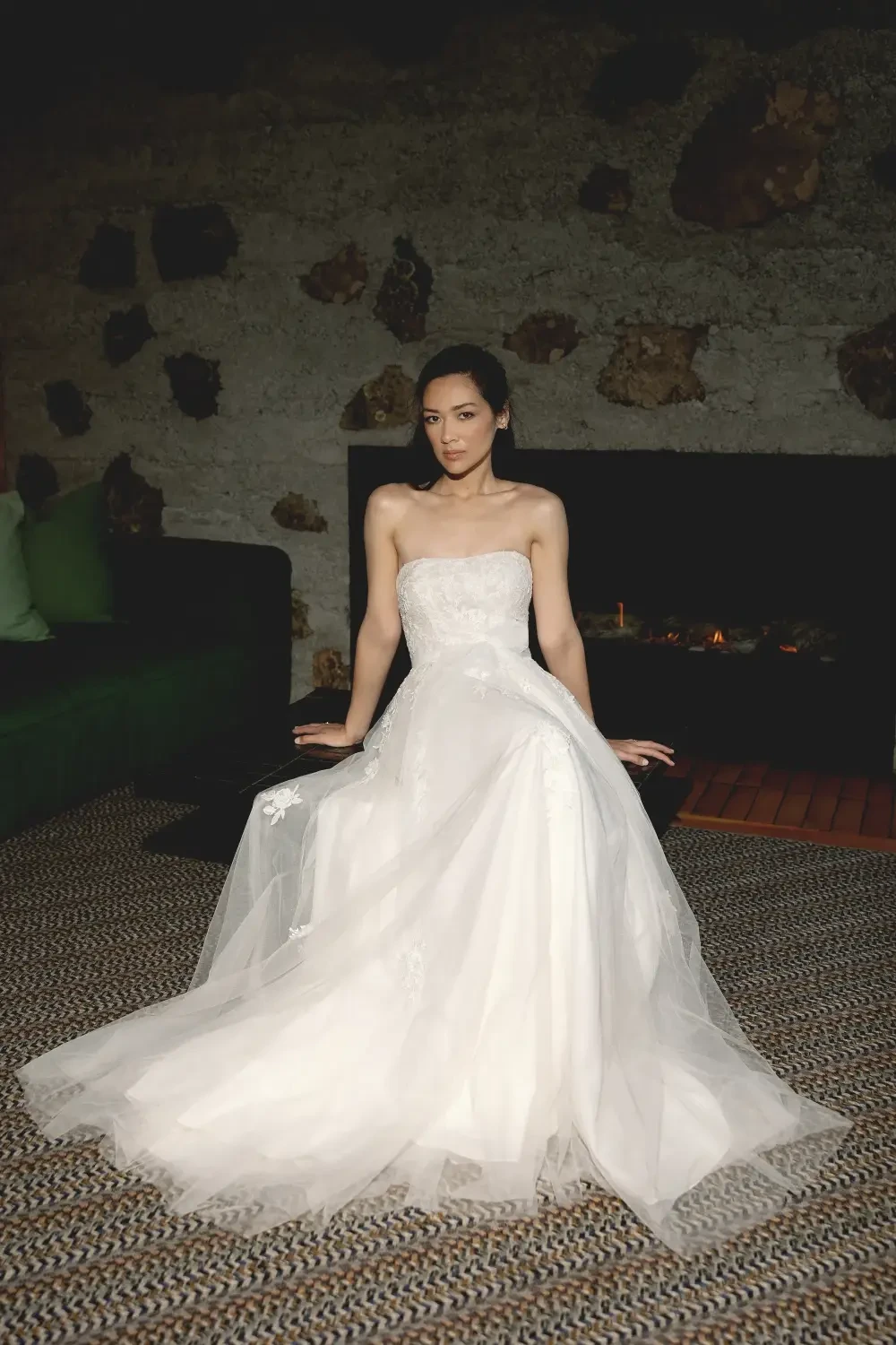 A woman in a strapless white wedding dress sitting gracefully on a floor.
