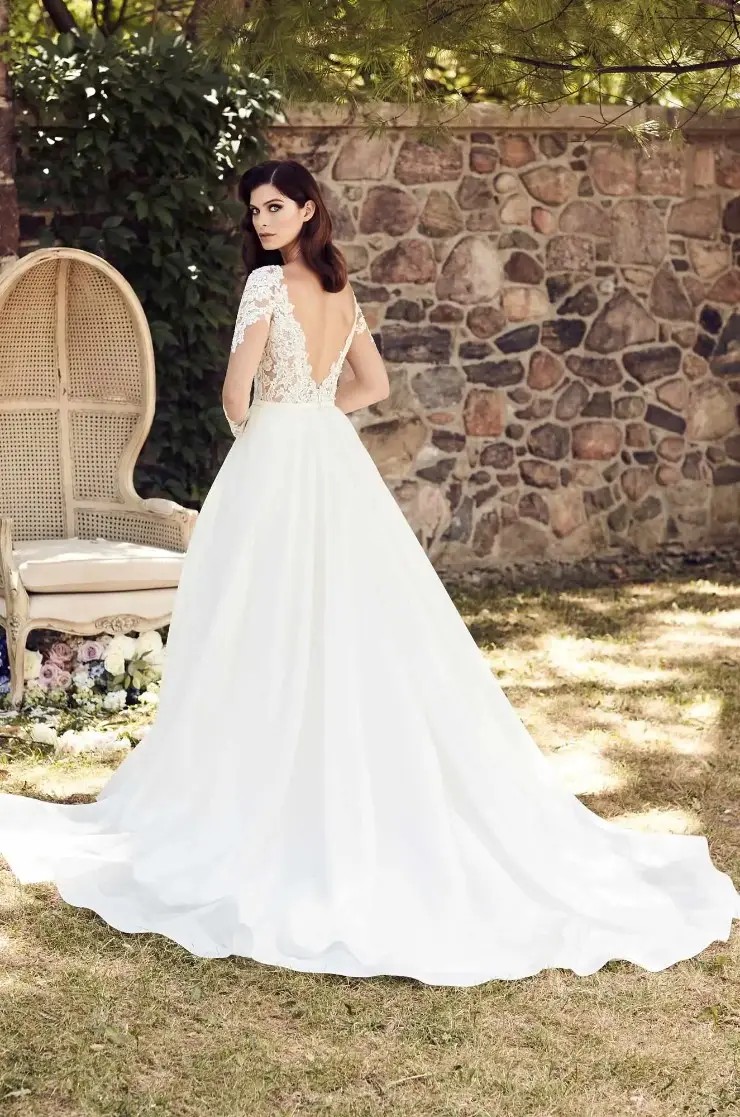 Model is wearing a romantic long sleeve A-line gown with an Alencon lace bodice, open back, and flowing organza skirt.