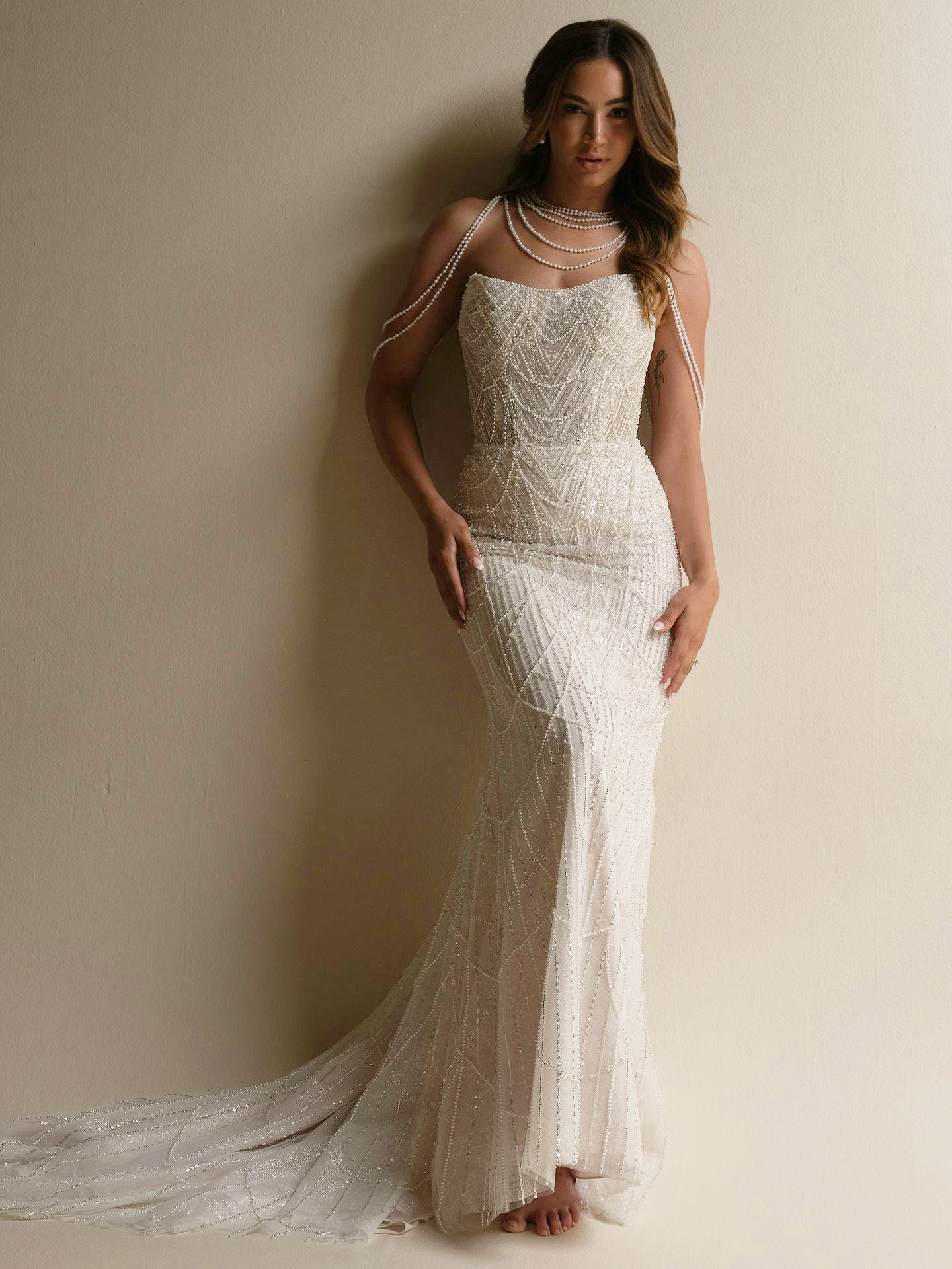 model is wearing a fitted wedding gown with pearls draped on the bodice