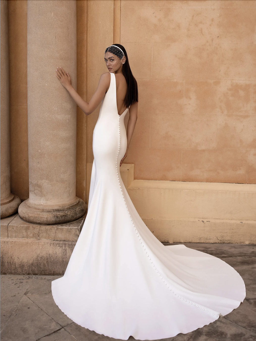 Model is wearing a sleek mermaid gown with a plunging V-neckline, sleeveless bodice, and a figure-hugging silhouette.