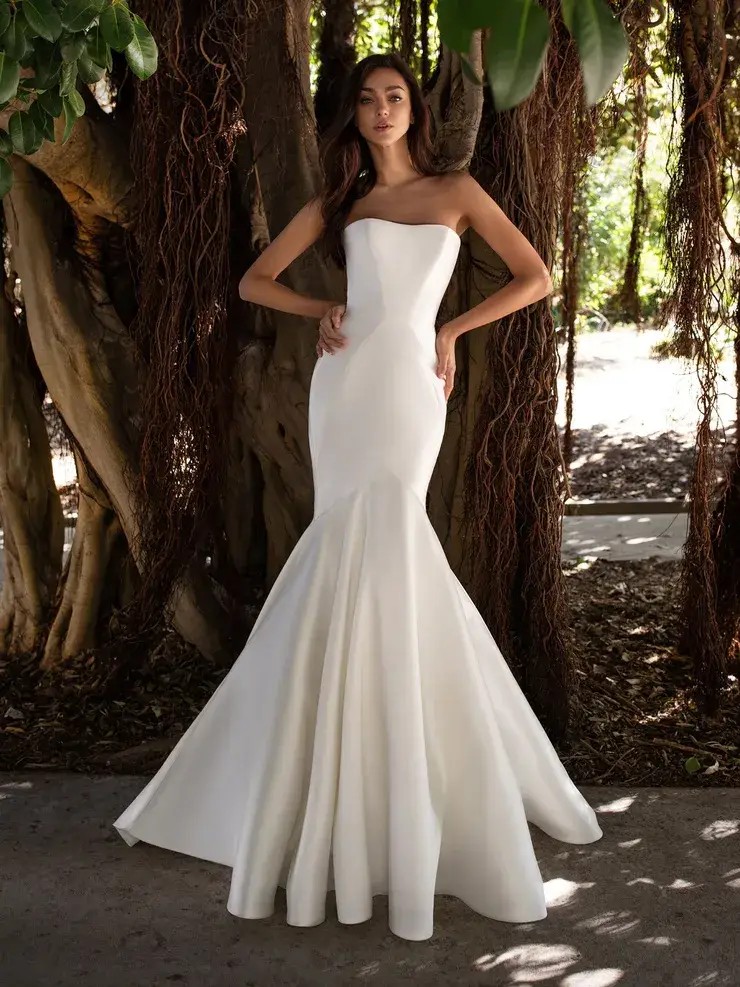 Model is wearing a strapless mikado trumpet gown with sculpted seams and elegant floor-length buttons trailing down the back.